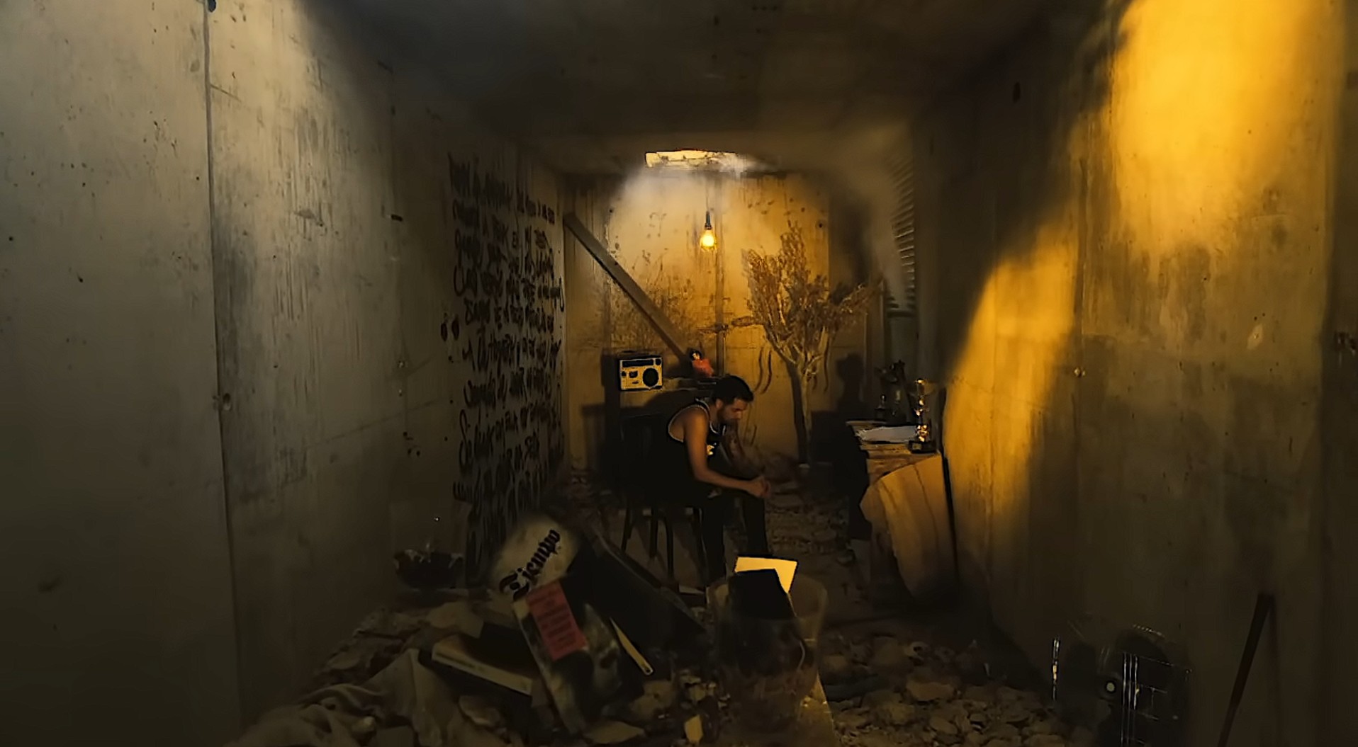 El cantante SHÉ sentado en una habitación en ruinas en el videoclip Sufrir es crecer